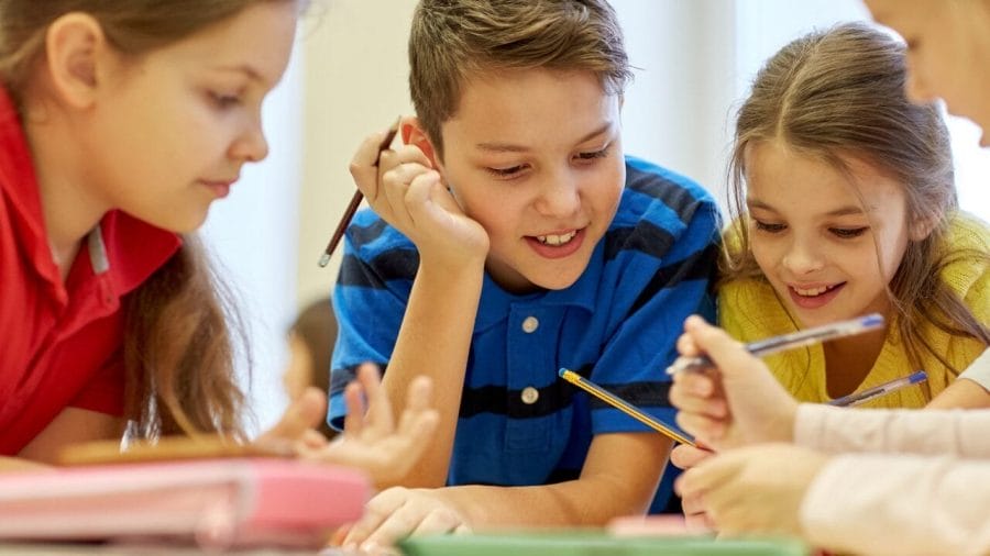 Gruppe von Schulkindern mit Stiften und Papier schreiben im Klassenzimmer